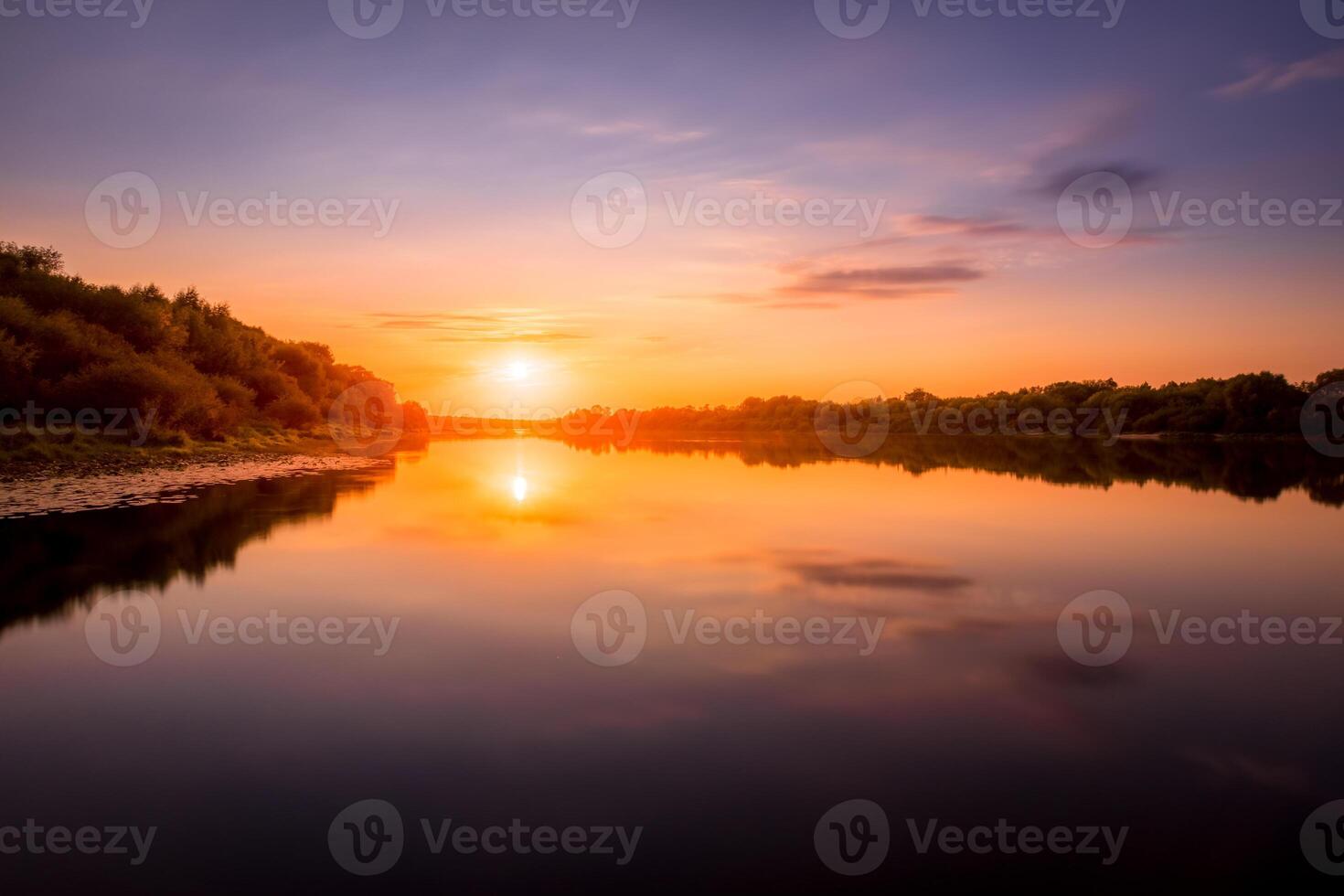 Sunset or dawn on a river with a cloudy sky and sun rays reflected in the water, water lilies and trees growing along the shore. photo