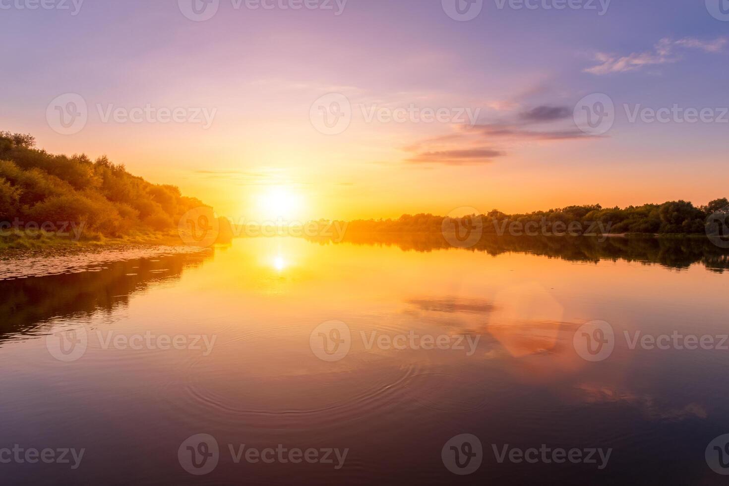 Sunset or dawn on a river with a cloudy sky and sun rays reflected in the water, water lilies and trees growing along the shore. photo