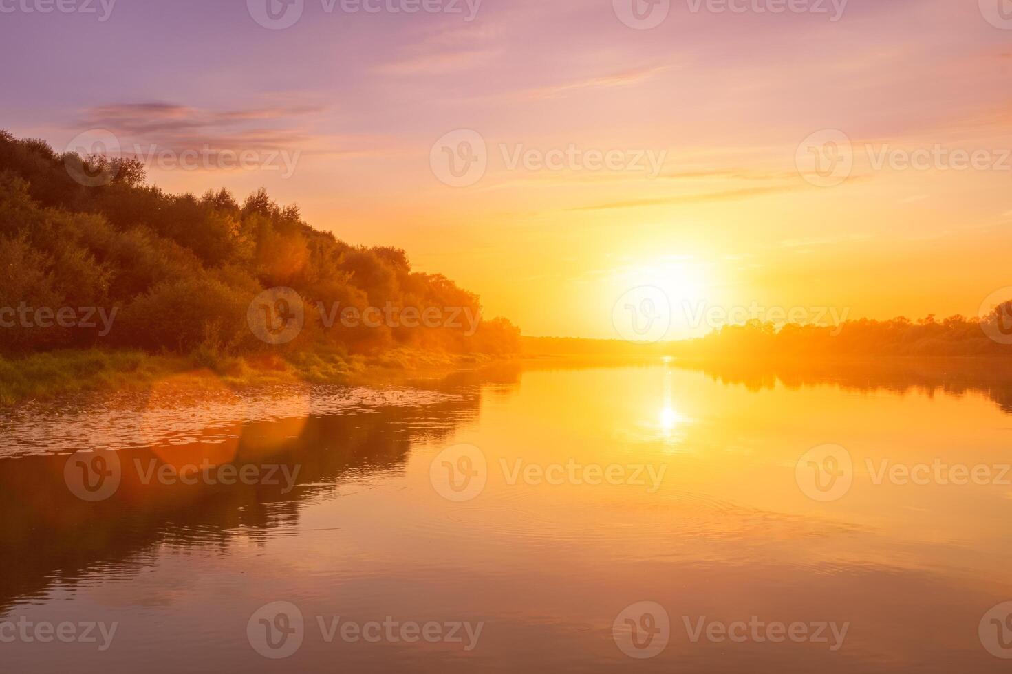 Sunset or dawn on a river with a cloudy sky and sun rays reflected in the water, water lilies and trees growing along the shore. photo