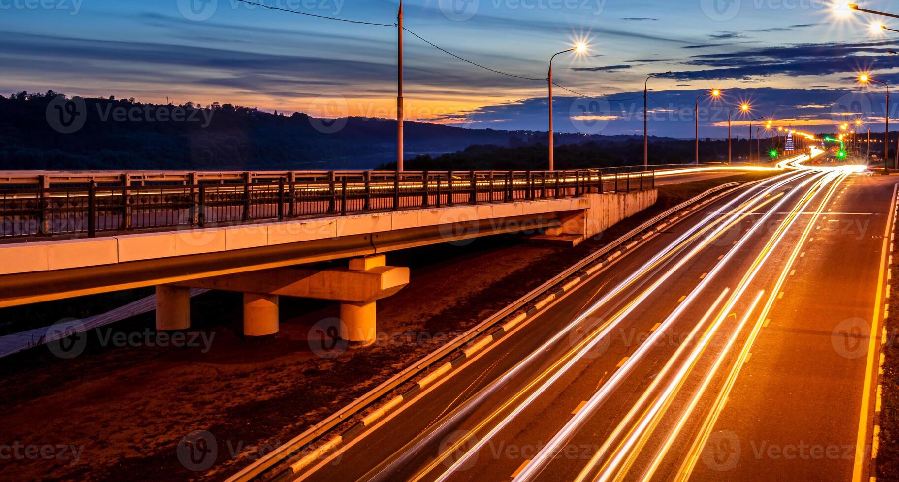 Traces of headlights from cars moving at night on the bridge, illuminated by lanterns. Abstract cityscape with highway at dusk. photo