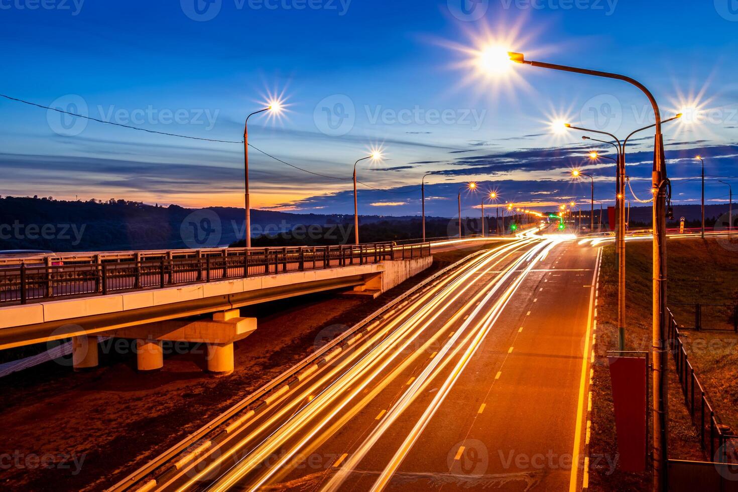Traces of headlights from cars moving at night on the bridge, illuminated by lanterns. Abstract cityscape with highway at dusk. photo