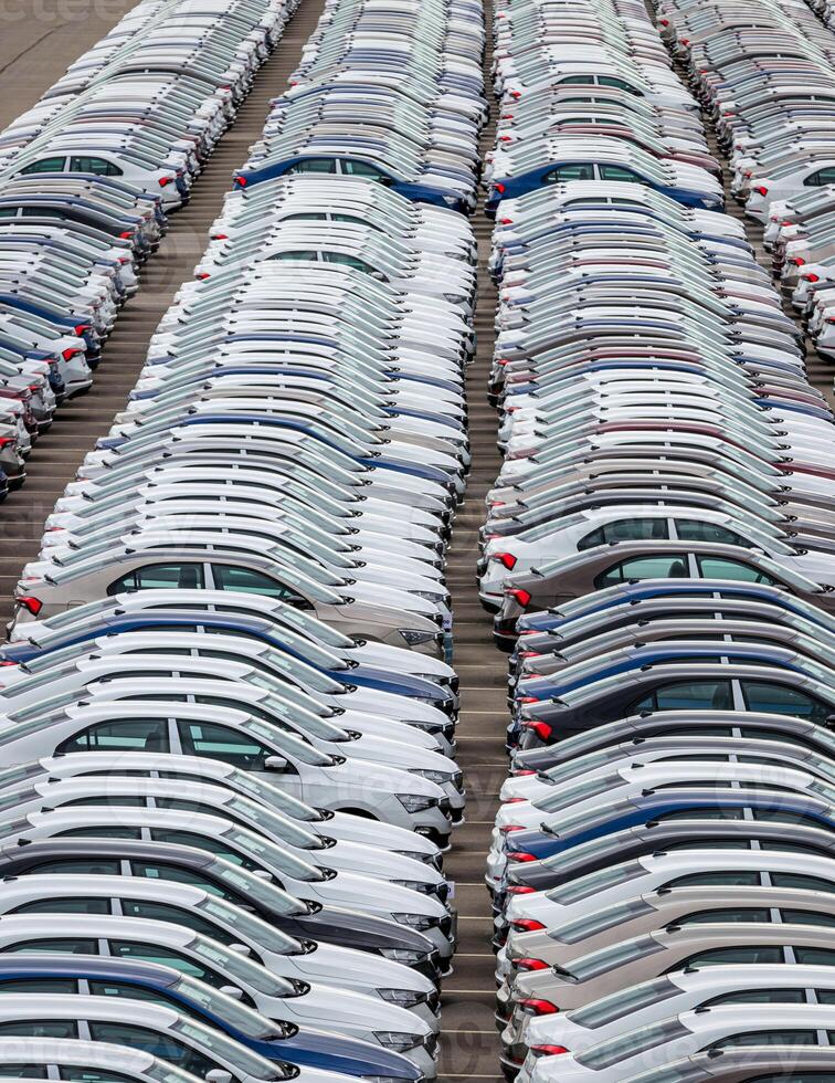 Rows of a new cars parked in a distribution center on a cloudy day in the spring, a car factory. Top view to the parking in the open air. photo