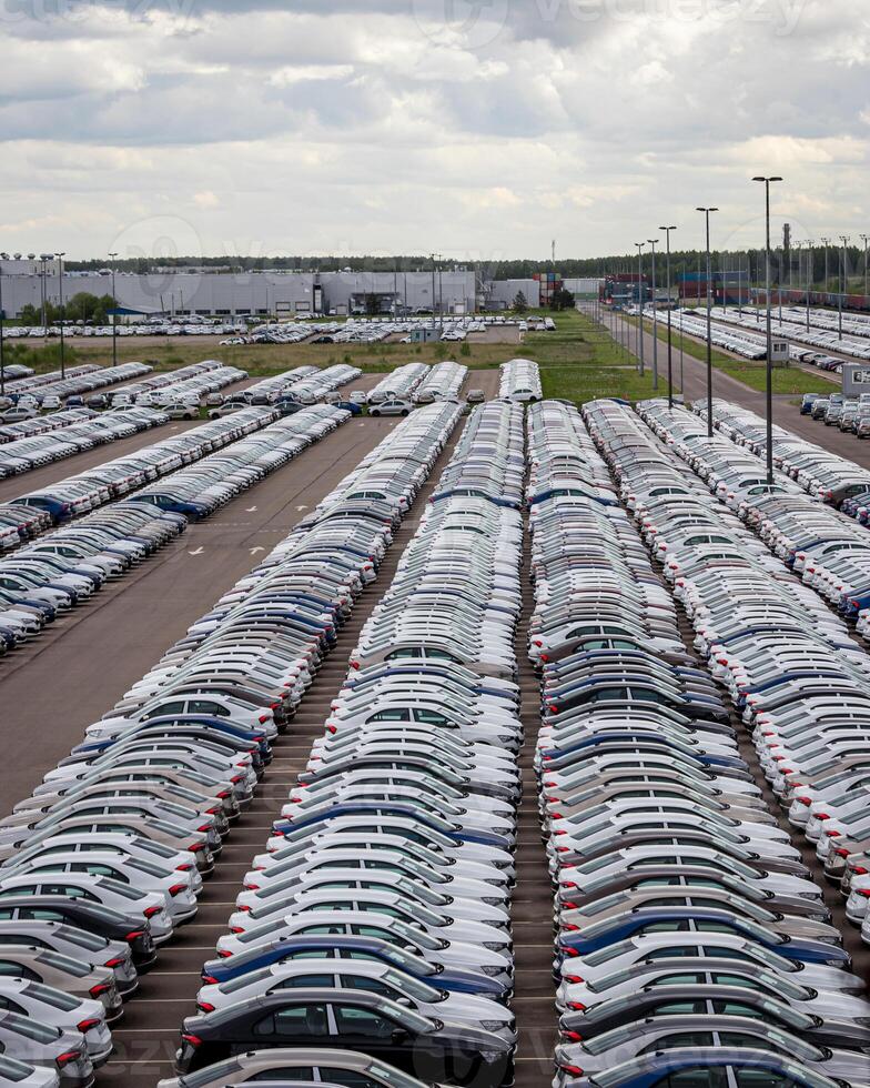 Rows of a new cars parked in a distribution center on a cloudy day in the spring, a car factory. Top view to the parking in the open air. photo