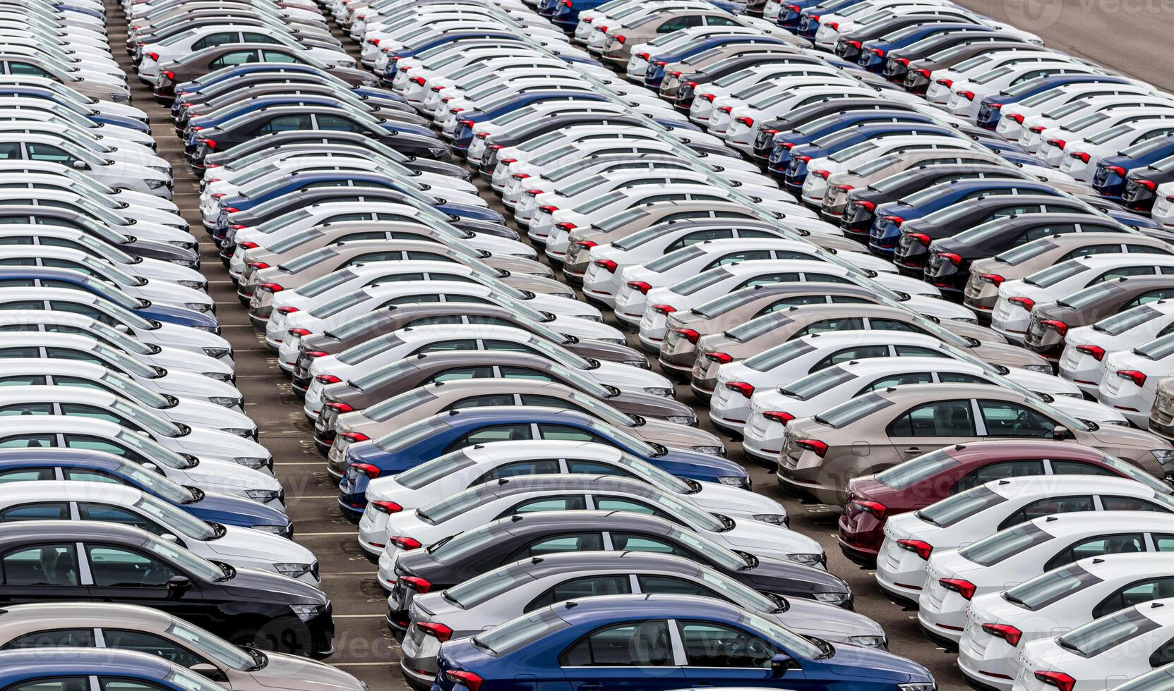 Rows of a new cars parked in a distribution center on a cloudy day in the spring, a car factory. Top view to the parking in the open air. photo