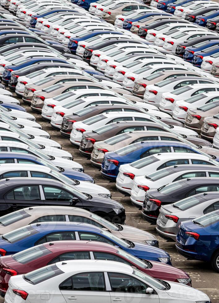 Rows of a new cars parked in a distribution center on a cloudy day in the spring, a car factory. Top view to the parking in the open air. photo