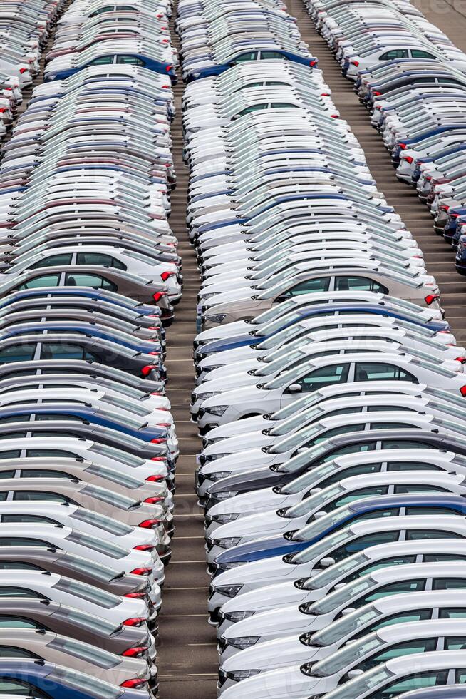 Rows of a new cars parked in a distribution center of a car factory. Top view to the parking in the open air. photo