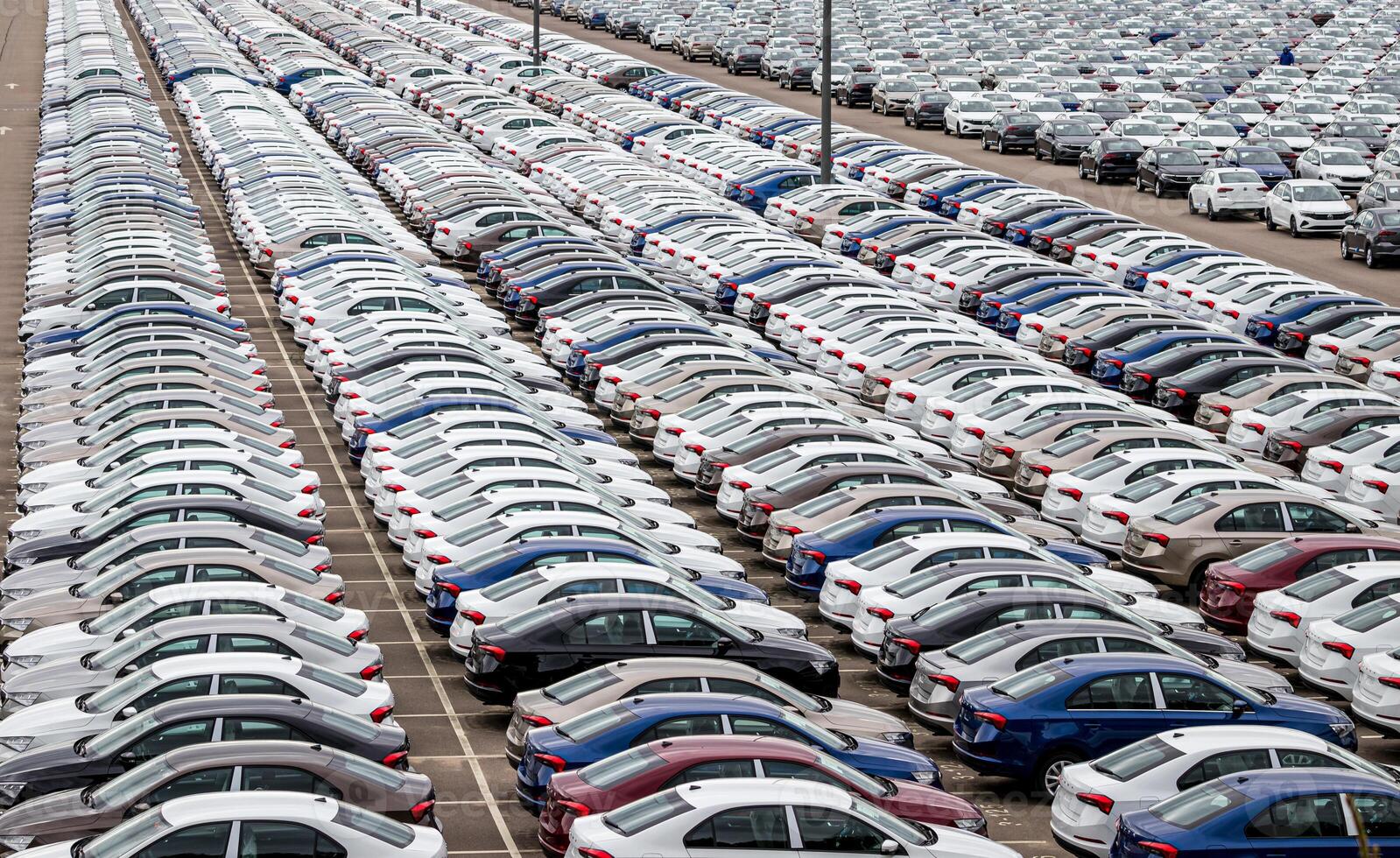 Rows of a new cars parked in a distribution center on a cloudy day in the spring, a car factory. Top view to the parking in the open air. photo