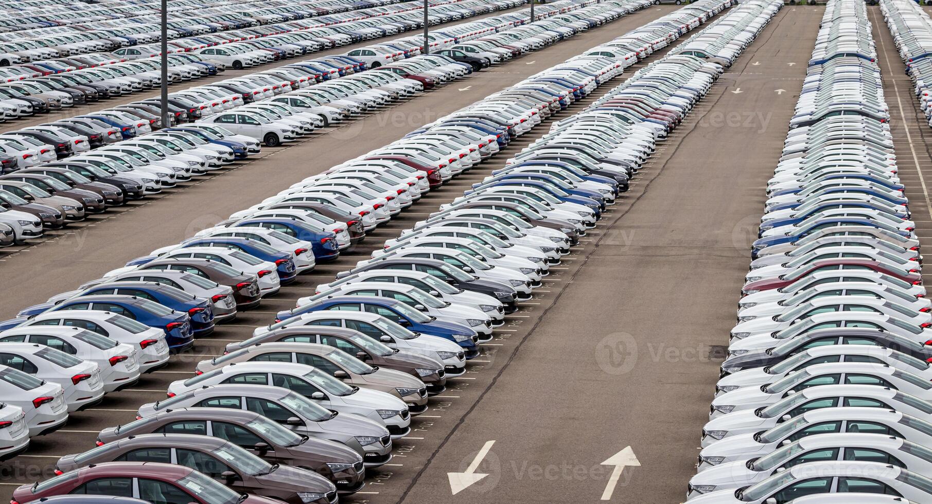 Rows of a new cars parked in a distribution center on a car factory on a cloudy day. Top view to the parking in the open air. photo