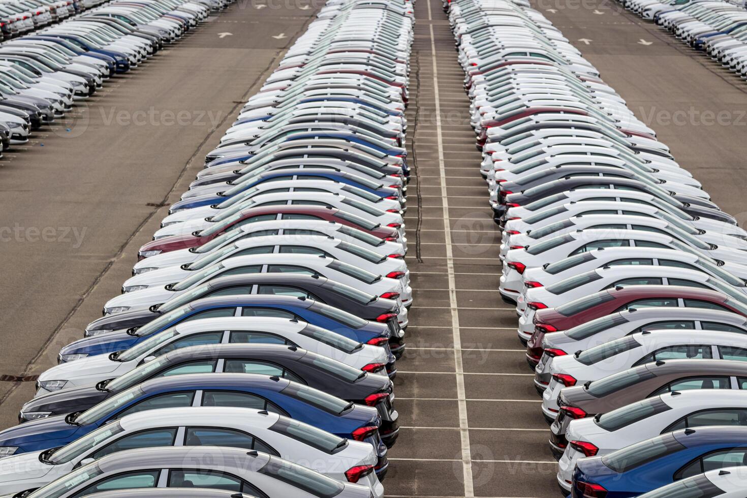 Rows of a new cars parked in a distribution center on a car factory on a cloudy day. Top view to the parking in the open air. photo
