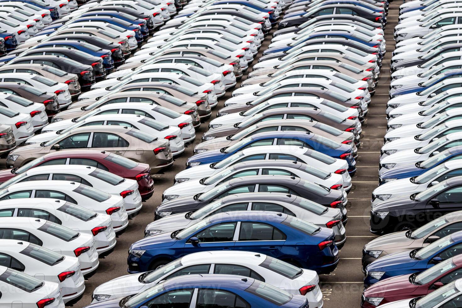 Rows of a new cars parked in a distribution center on a cloudy day in the spring, a car factory. Top view to the parking in the open air. photo