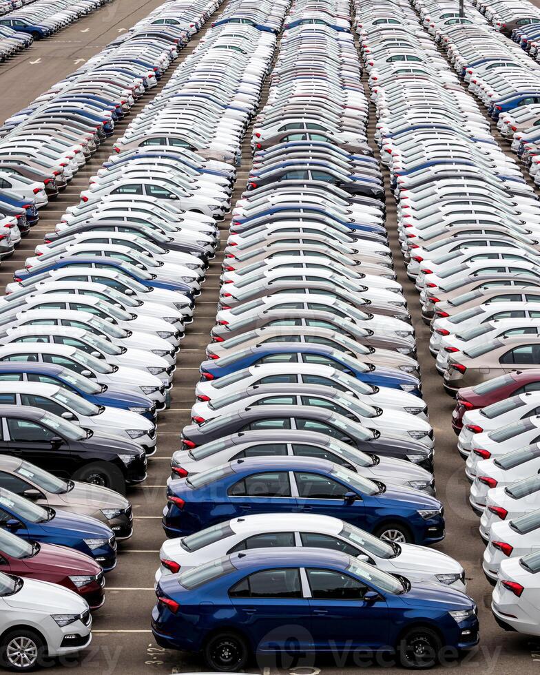 Rows of a new cars parked in a distribution center on a cloudy day in the spring, a car factory. Top view to the parking in the open air. photo