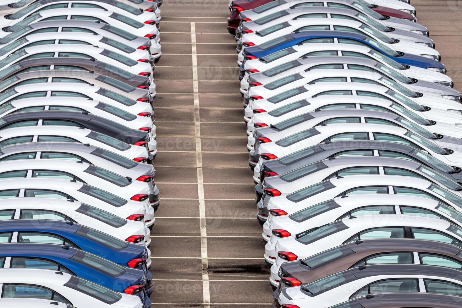 Rows of a new cars parked in a distribution center on a car factory on a cloudy day. Top view to the parking in the open air. photo