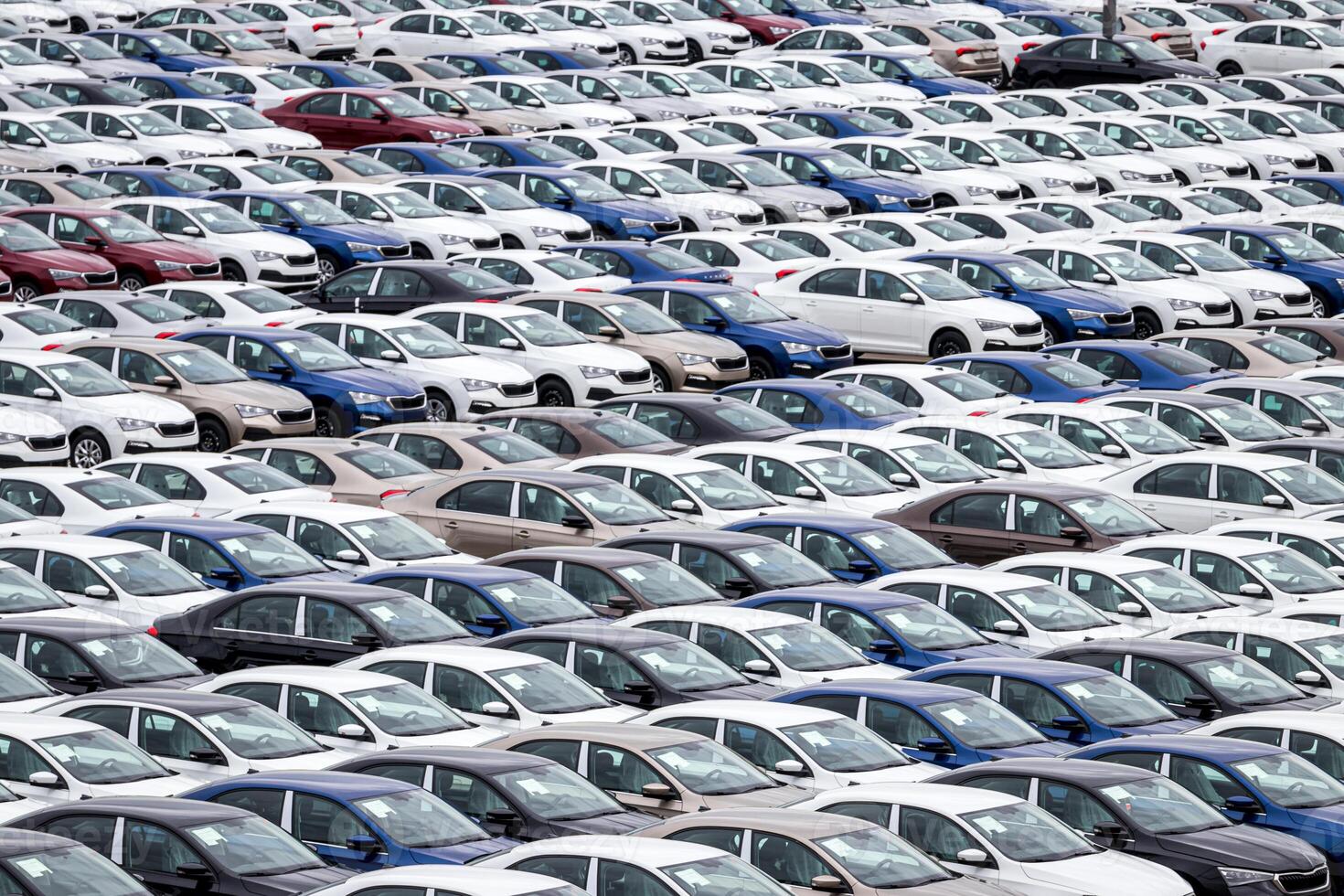 Rows of a new cars parked in a distribution center on a car factory on a cloudy day. Top view to the parking in the open air. photo
