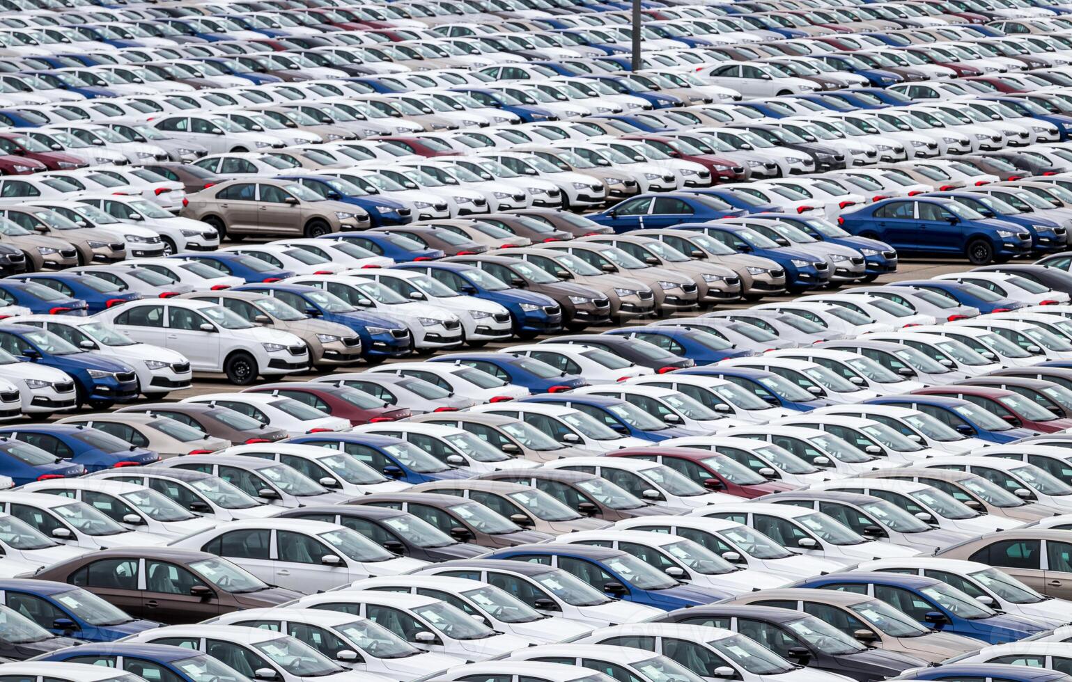 Rows of a new cars parked in a distribution center on a cloudy day in the spring, a car factory. Top view to the parking in the open air. photo