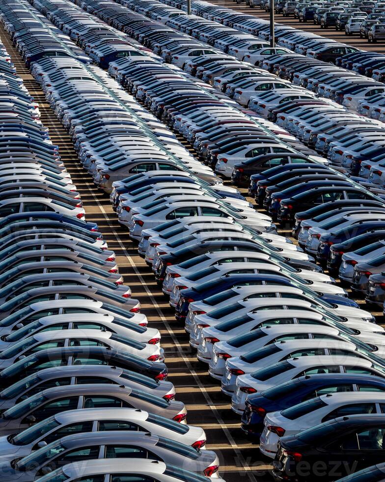 Rows of a new cars parked in a distribution center on a car factory on a sunny day. Top view to the parking in the open air. photo