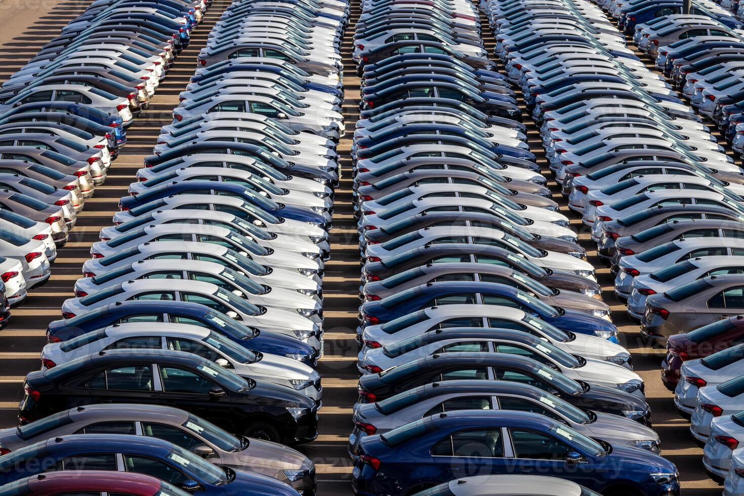 Rows of a new cars parked in a distribution center on a car factory on a sunny day. Top view to the parking in the open air. photo