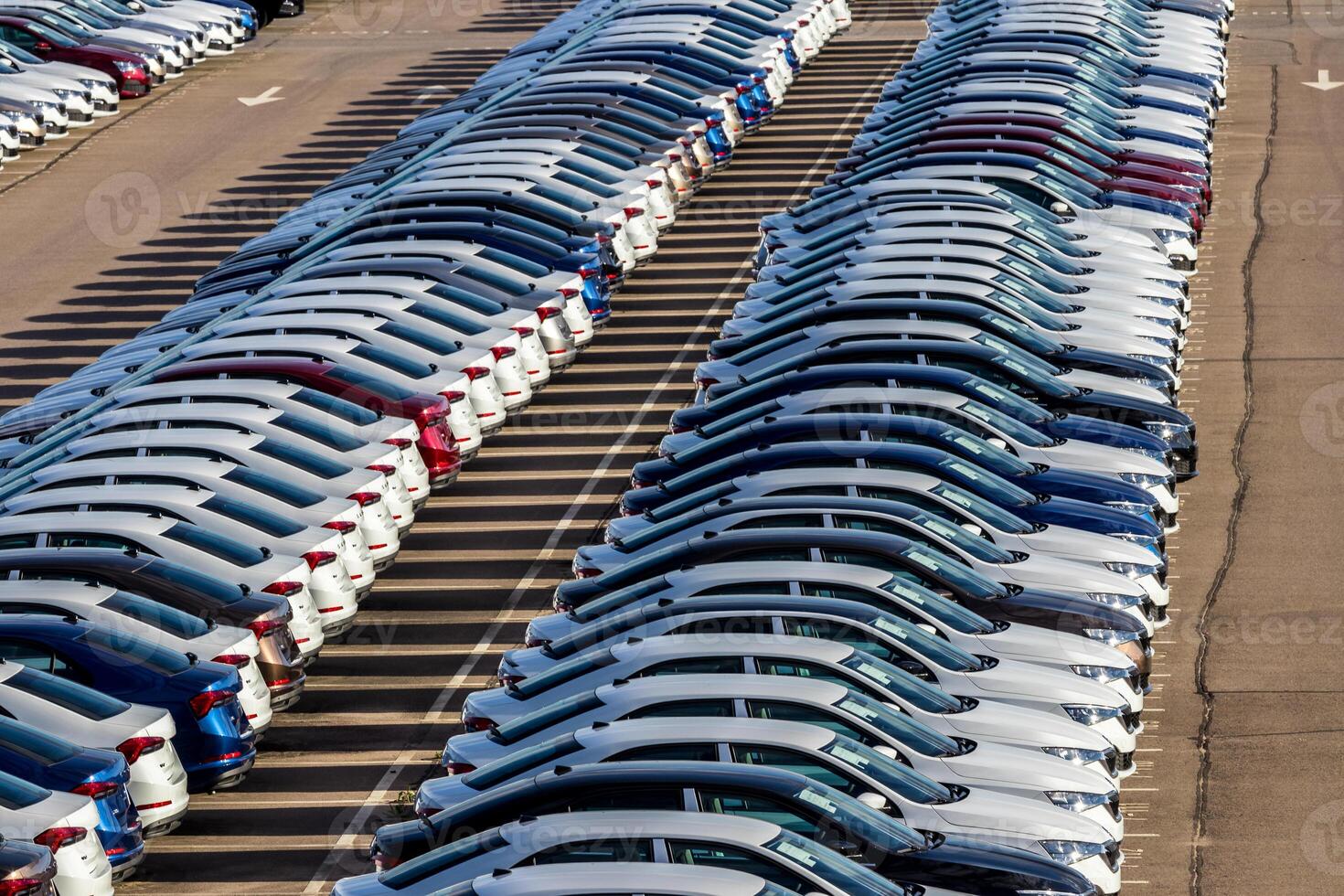 Rows of a new cars parked in a distribution center on a car factory on a sunny day. Top view to the parking in the open air. photo