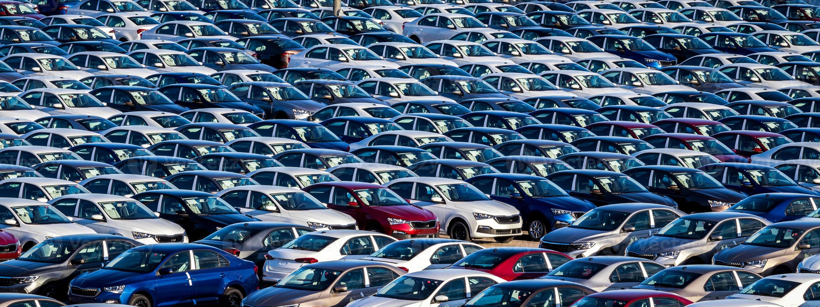Rows of a new cars parked in a distribution center on a car factory on a sunny day. Top view to the parking in the open air. photo