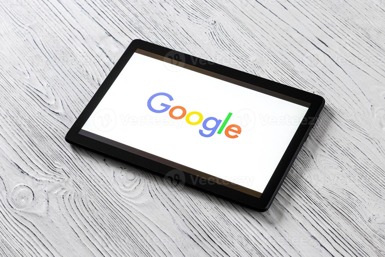 Black tablet computer on a white wooden table with a search system google logo on the screen. photo