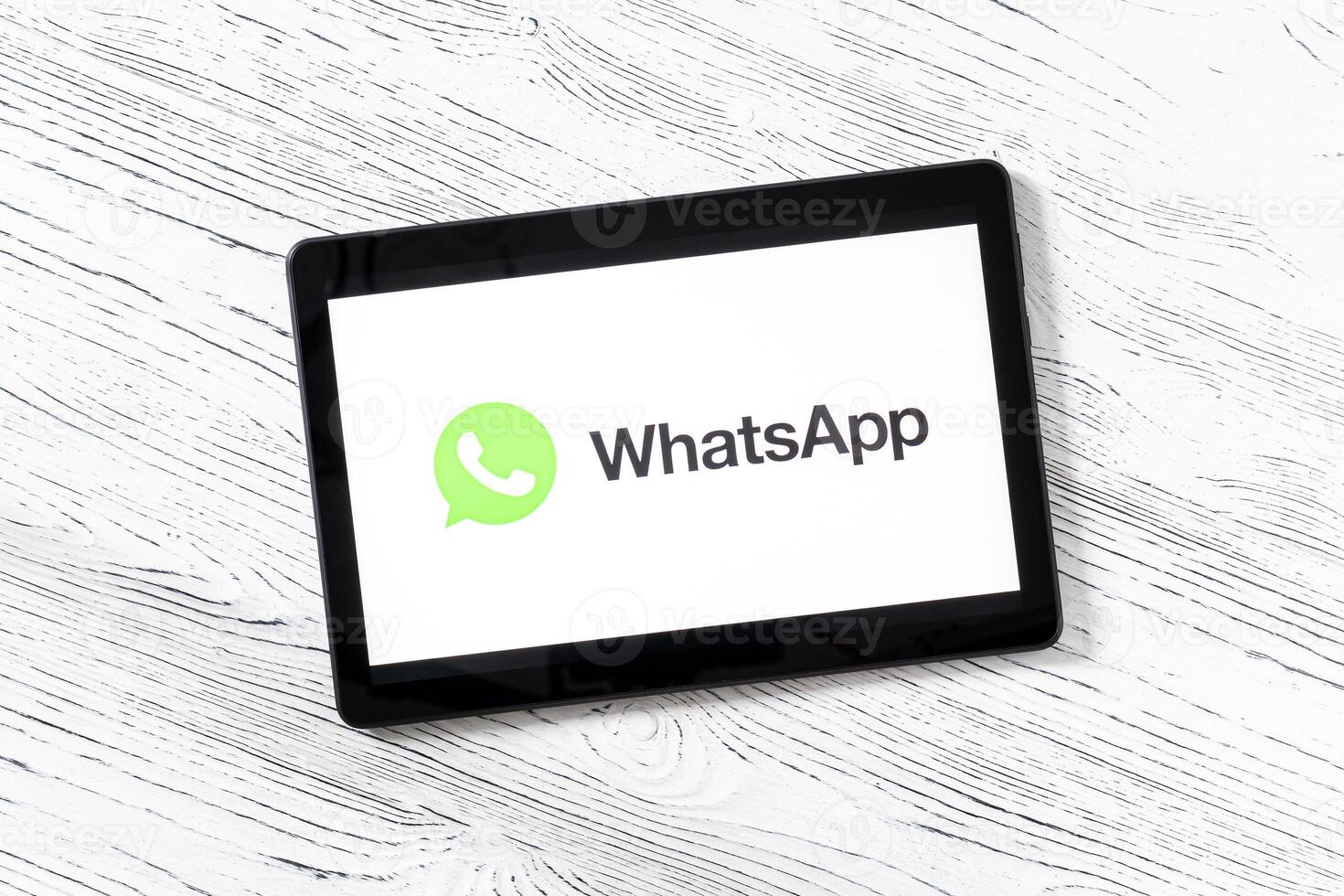 Black tablet computer on a white wooden table with a messenger WhatsApp logo on the screen. photo