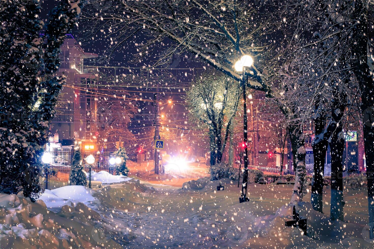 Winter night park with lanterns, pavement and trees covered with snow in snowfall. photo