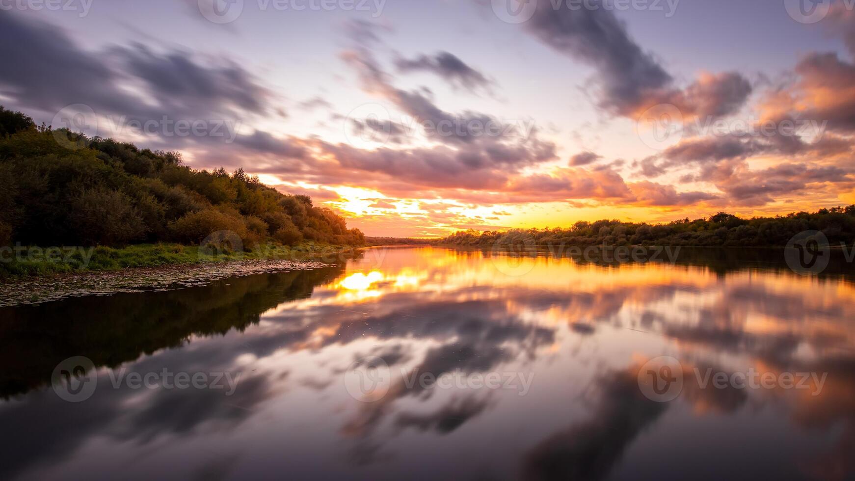 A sunset or sunrise scene over a lake or river with dramatic cloudy skies reflecting in the water on a summer evening or morning. photo
