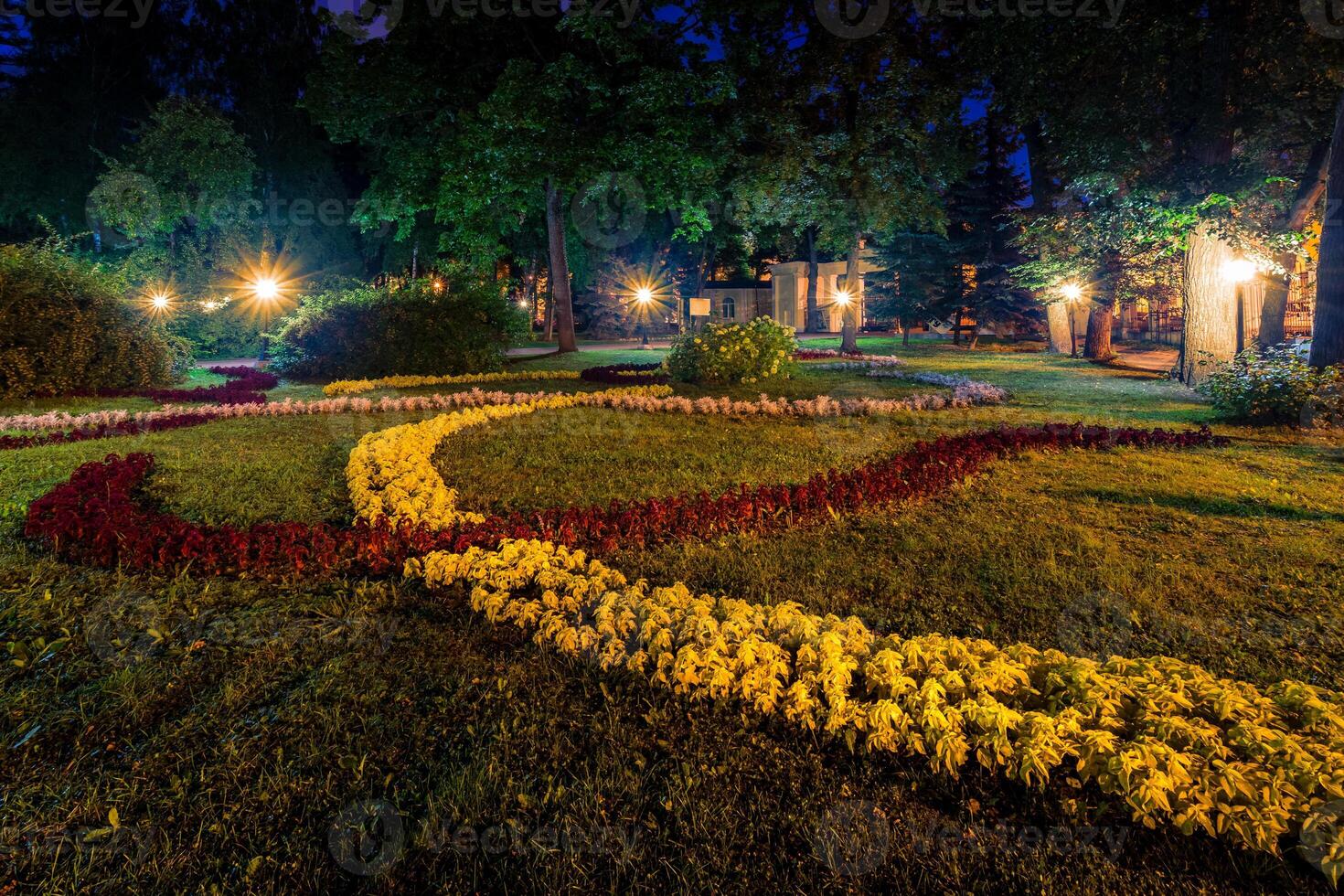 A night park lit by lanterns with a stone pavement, trees, fallen leaves and benches in early autumn. photo