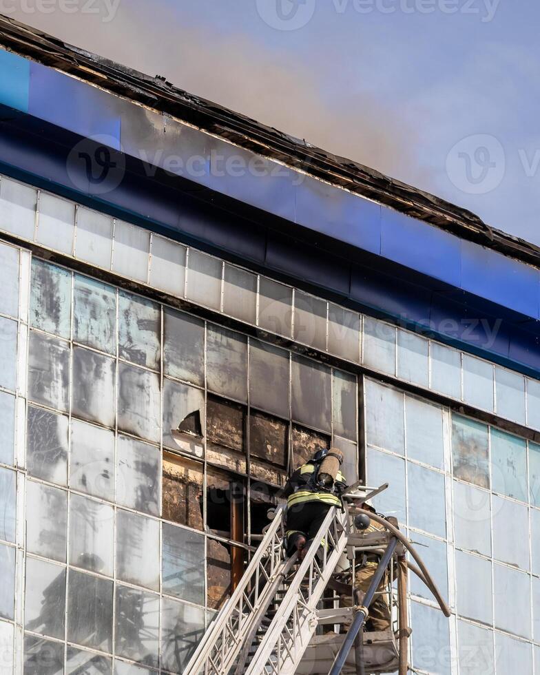 Russia, Kaluga - SEPTEMBER 08, 2020 A team of firefighters in protective suits and helmets on the stairs extinguishing a fire in a building with a broken window. photo