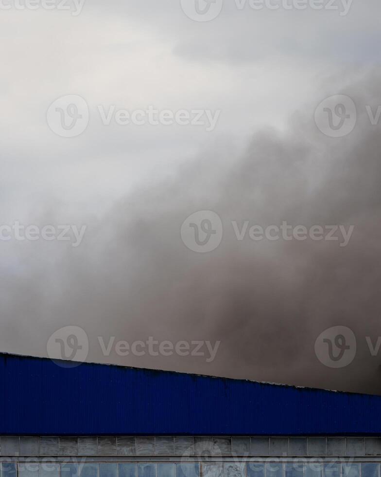 Black smoke rising from a burning building with a cloudy sky. photo