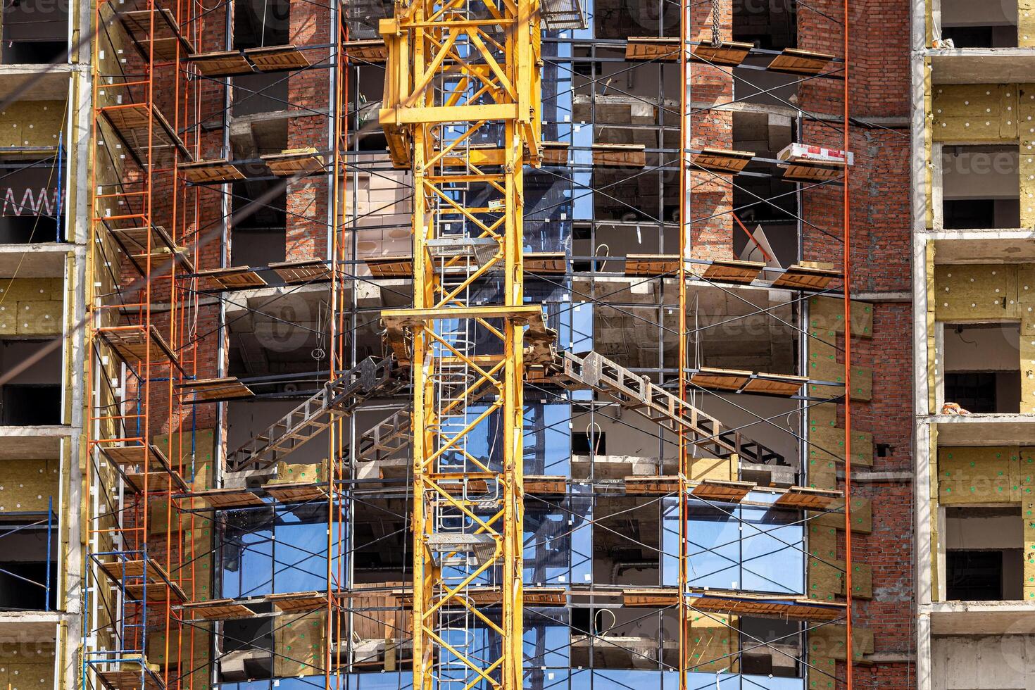 Fragment of an unfinished concrete and brick building under construction with scaffolding and a crane. photo