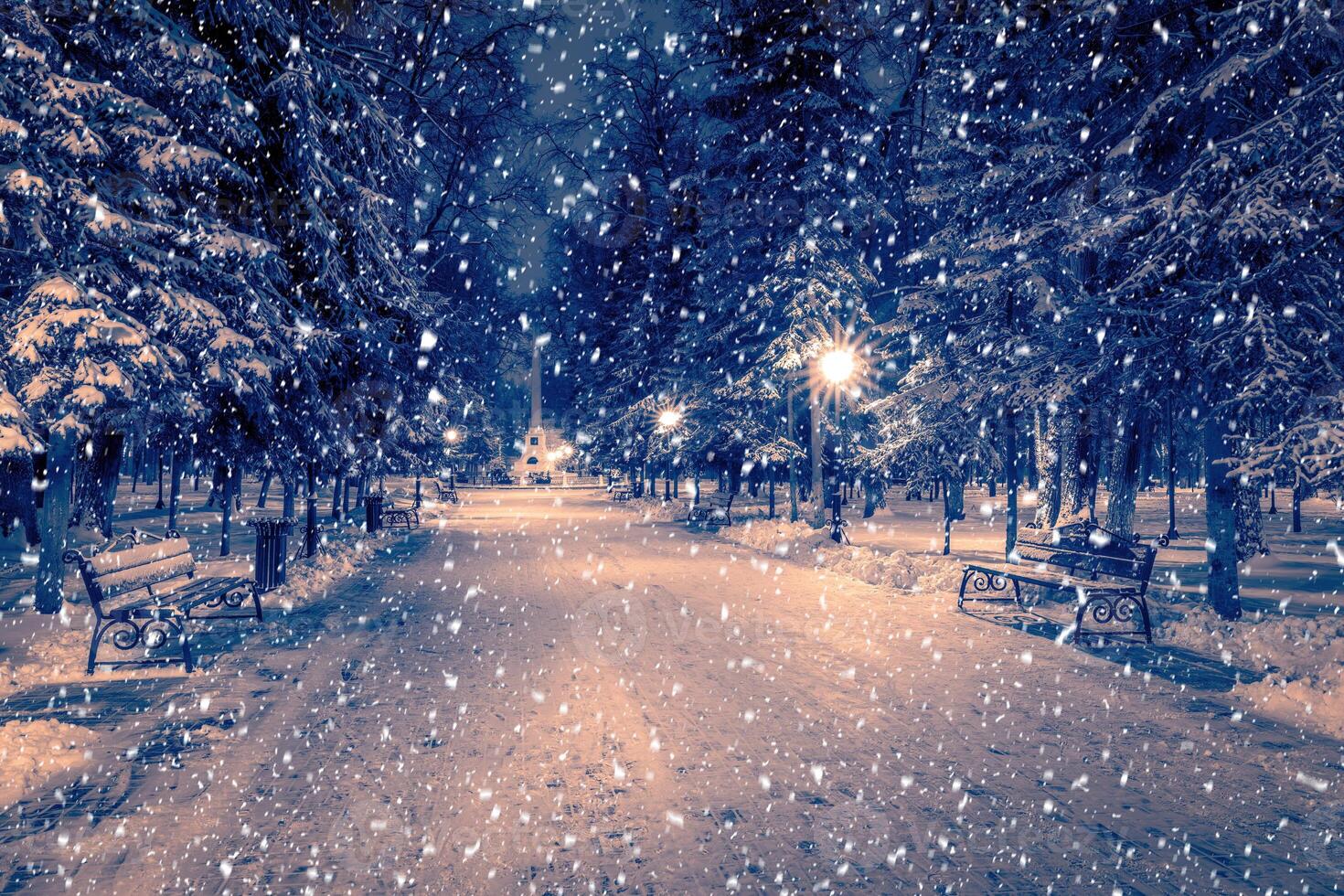 Snowfall in a winter park at night with christmas decorations, lights and pavement covered with snow. photo
