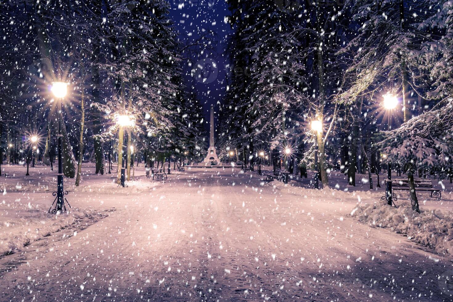 Snowfall in a winter park at night with christmas decorations, lights and pavement covered with snow. photo