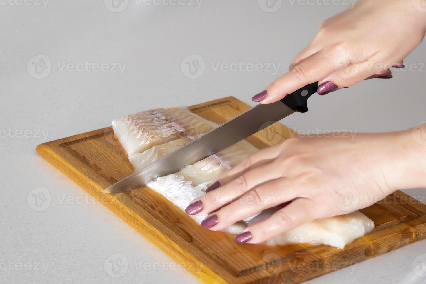 Female hands cutting fish meat with a knife on a cutting board. photo