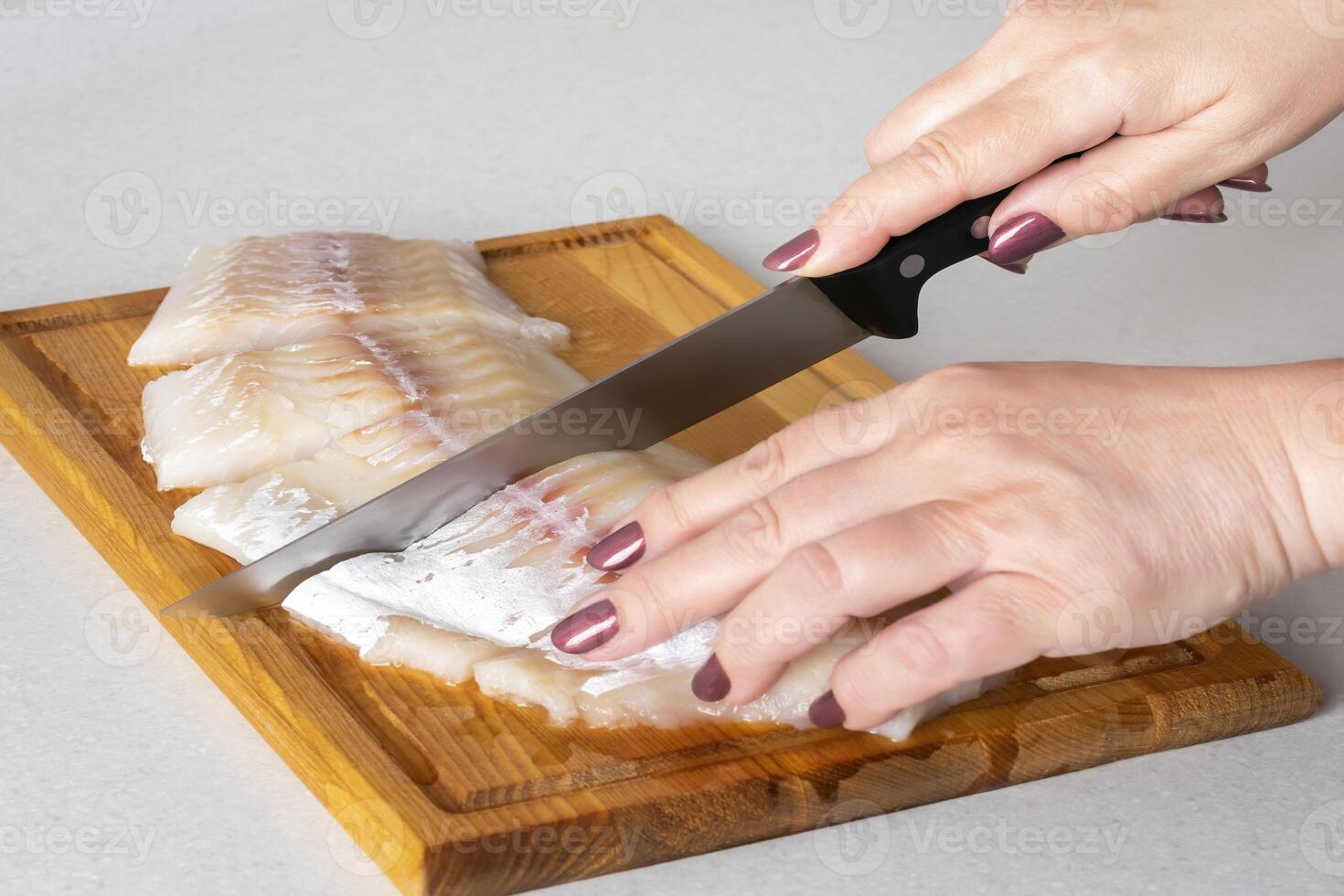 Female hands cutting fish meat with a knife on a cutting board. photo