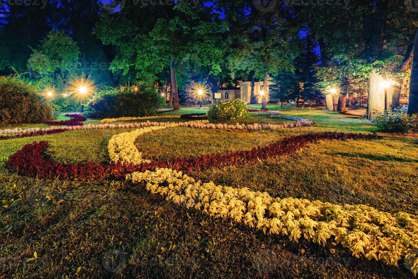 A night park lit by lanterns with a stone pavement, trees, fallen leaves and benches in early autumn. photo