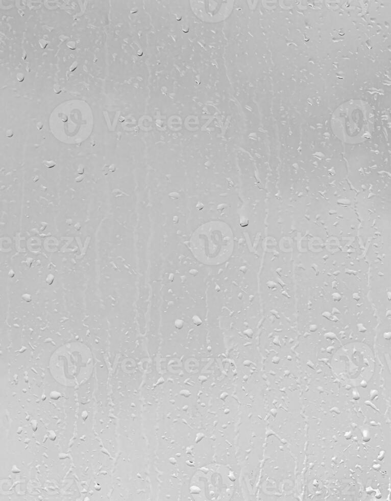Rain drops on window glasses surface with gray sky background. Natural backdrop of raindrops. The concept of bad rainy weather. photo