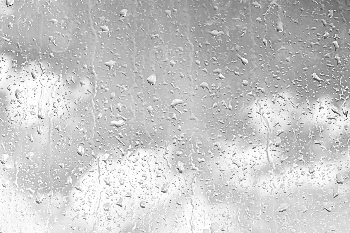 Rain drops on window glasses surface with gray sky background. Natural backdrop of raindrops. The concept of bad rainy weather. photo