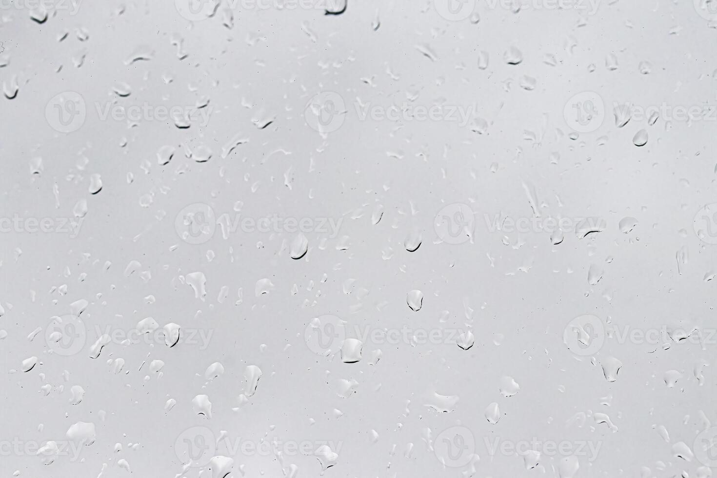Rain drops on window glasses surface with gray sky background. Natural backdrop of raindrops. The concept of bad rainy weather. photo