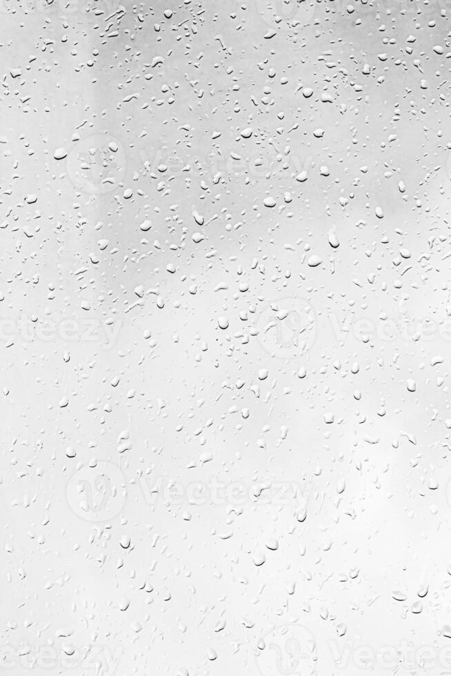 Rain drops on window glasses surface with gray sky background. Natural backdrop of raindrops. The concept of bad rainy weather. photo