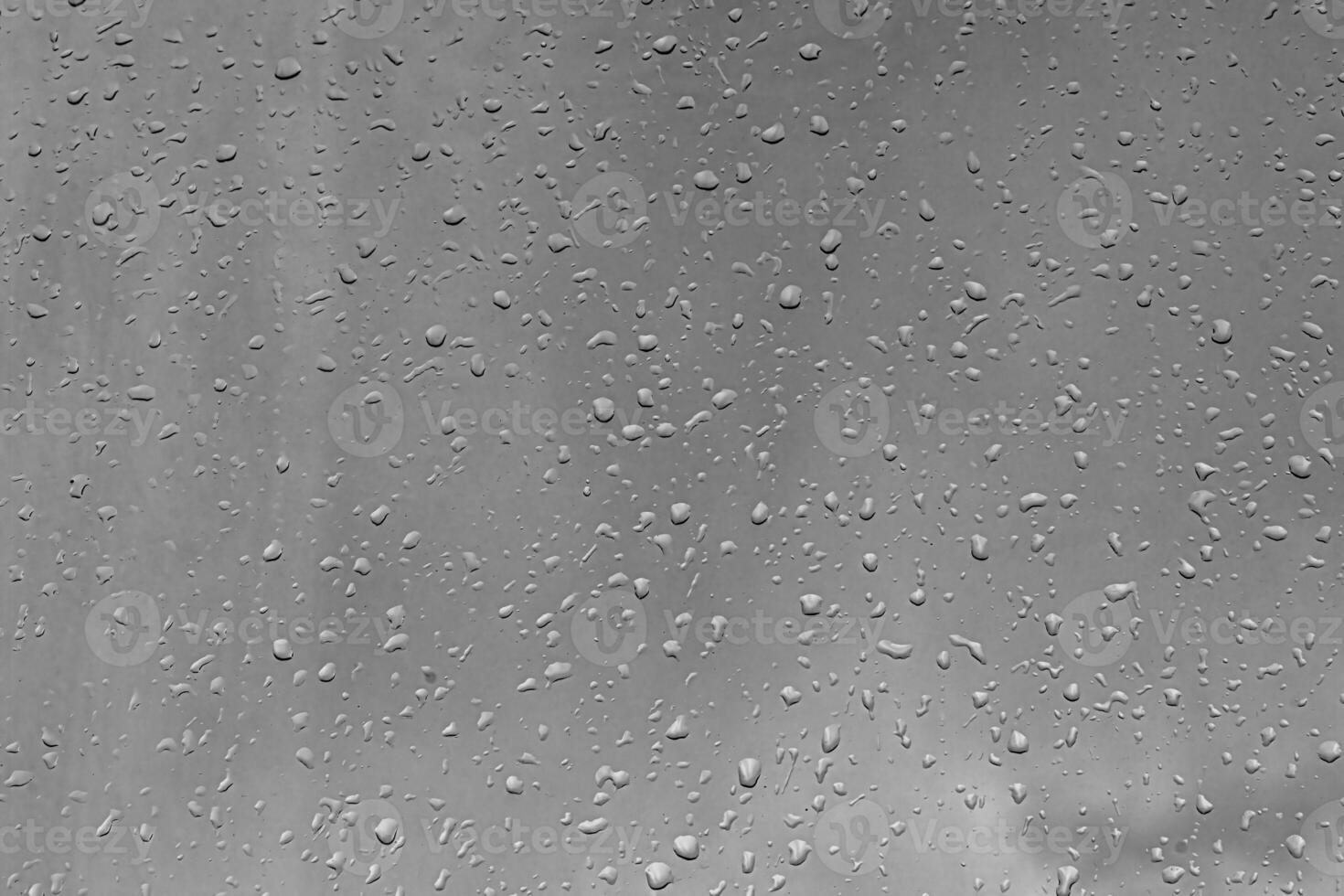 Rain drops on window glasses surface with gray sky background. Natural backdrop of raindrops. The concept of bad rainy weather. photo