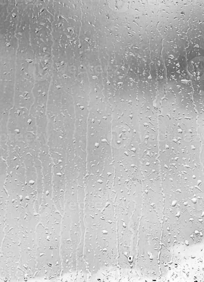 Rain drops on window glasses surface with gray sky background. Natural backdrop of raindrops. The concept of bad rainy weather. photo