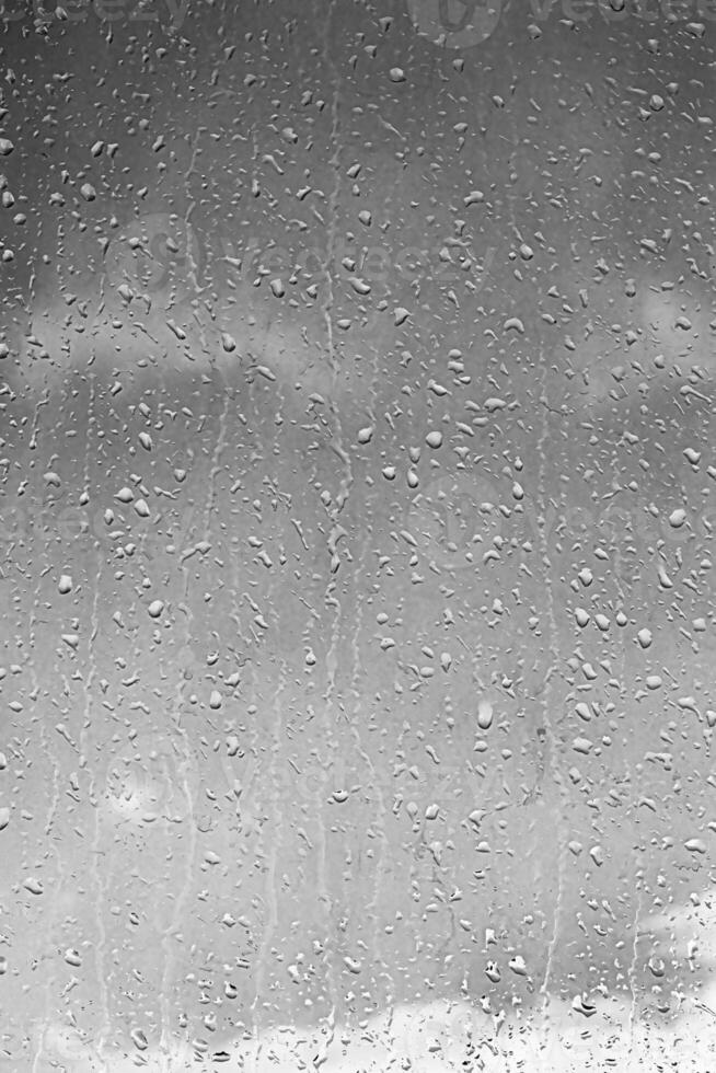 Rain drops on window glasses surface with gray sky background. Natural backdrop of raindrops. The concept of bad rainy weather. photo