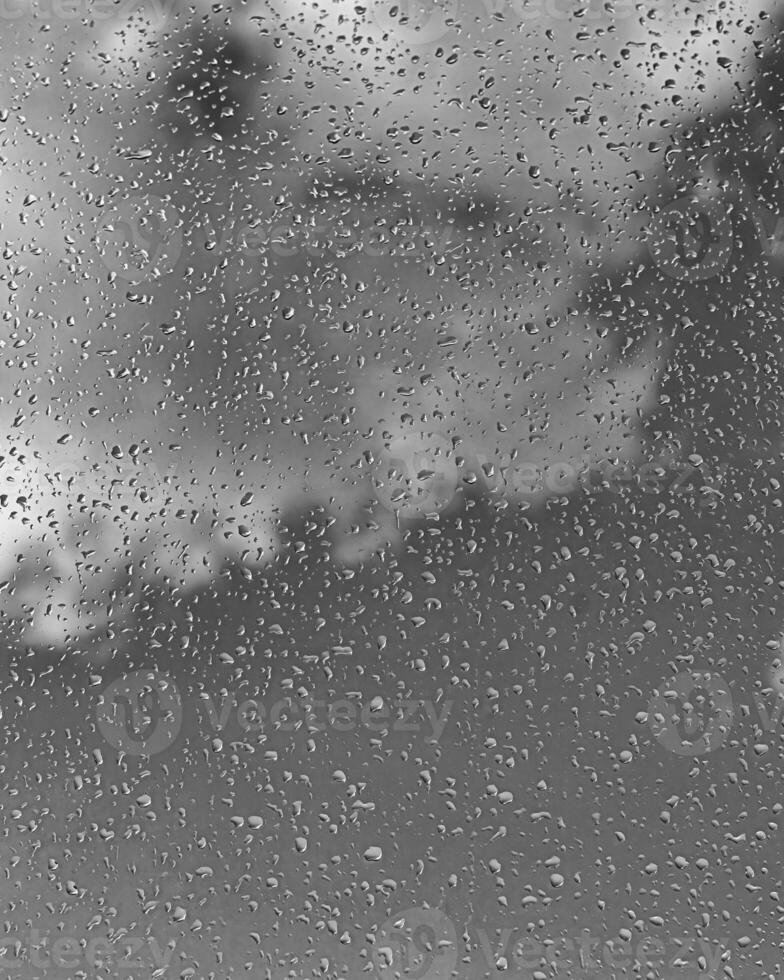Rain drops on window glasses surface with gray sky background. Natural backdrop of raindrops. The concept of bad rainy weather. photo