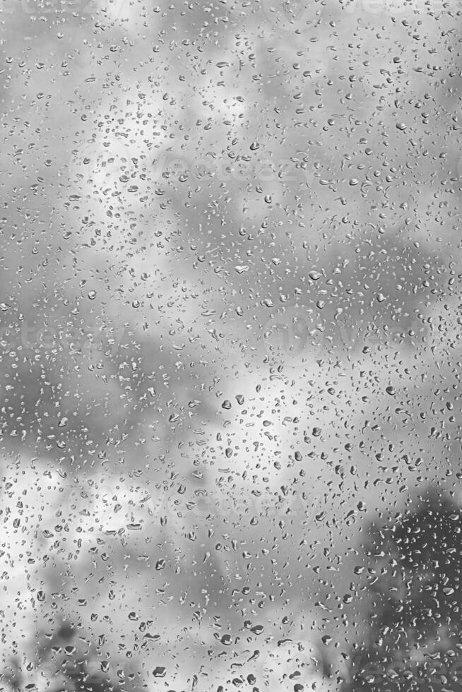 Rain drops on window glasses surface with gray sky background. Natural backdrop of raindrops. The concept of bad rainy weather. photo