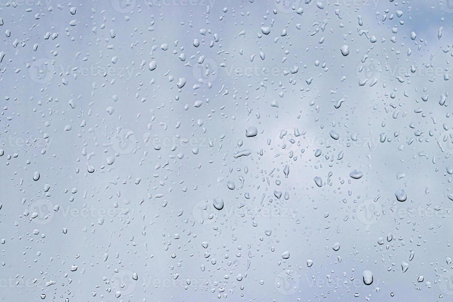 Rain drops on window glasses surface with gray sky background. Natural backdrop of raindrops. The concept of bad rainy weather. photo