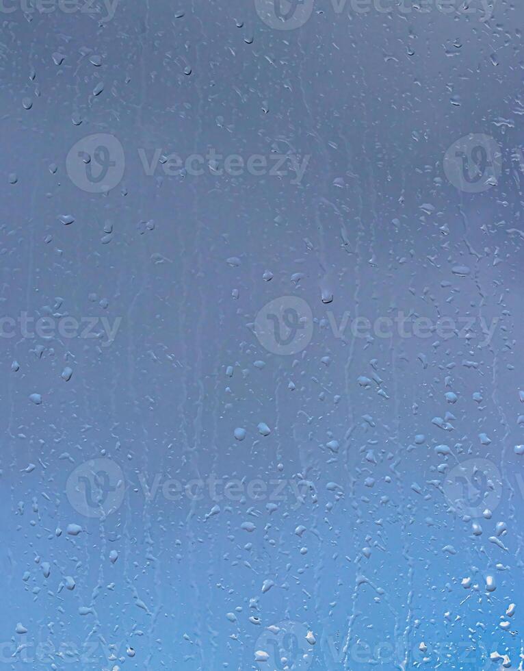 Rain drops on window glasses surface with blue sky and clouds background. Raindrops on a glass. The concept of changing from rainy to sunny weather. photo