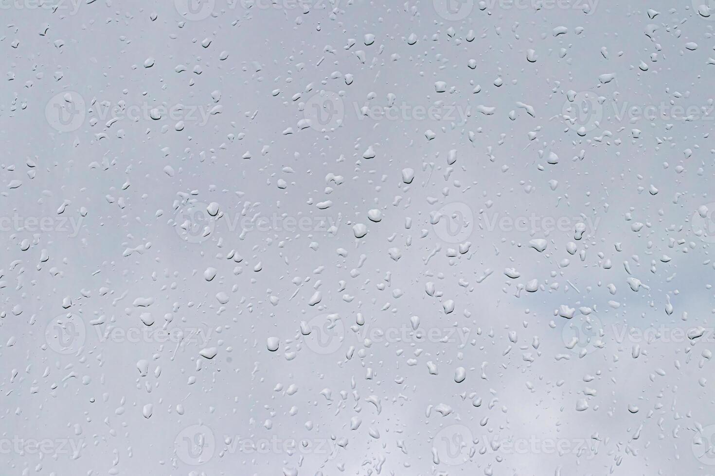 Rain drops on window glasses surface with gray sky background. Natural backdrop of raindrops. The concept of bad rainy weather. photo