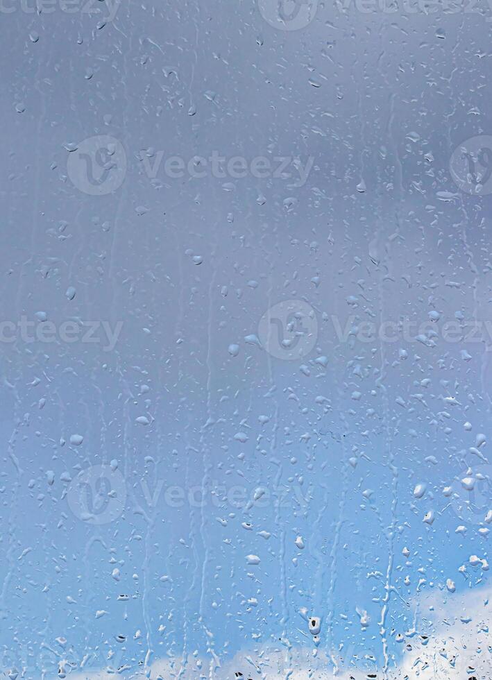 Rain drops on window glasses surface with blue sky and clouds background. Raindrops on a glass. The concept of changing from rainy to sunny weather. photo