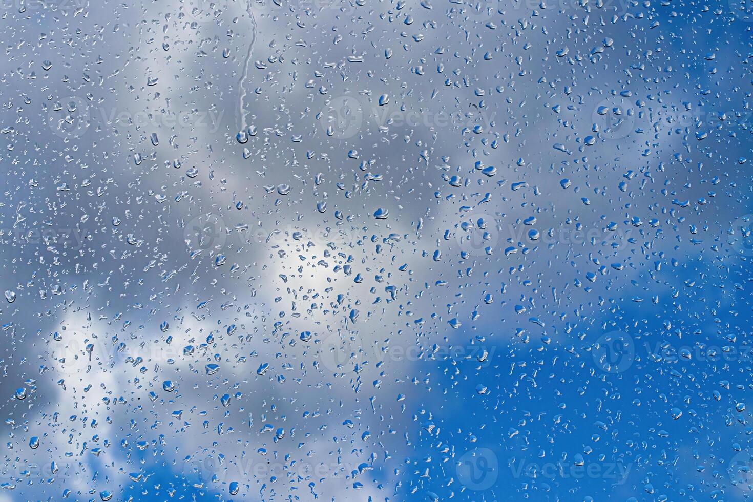Rain drops on window glasses surface with blue sky and clouds background. Raindrops on a glass. The concept of changing from rainy to sunny weather. photo
