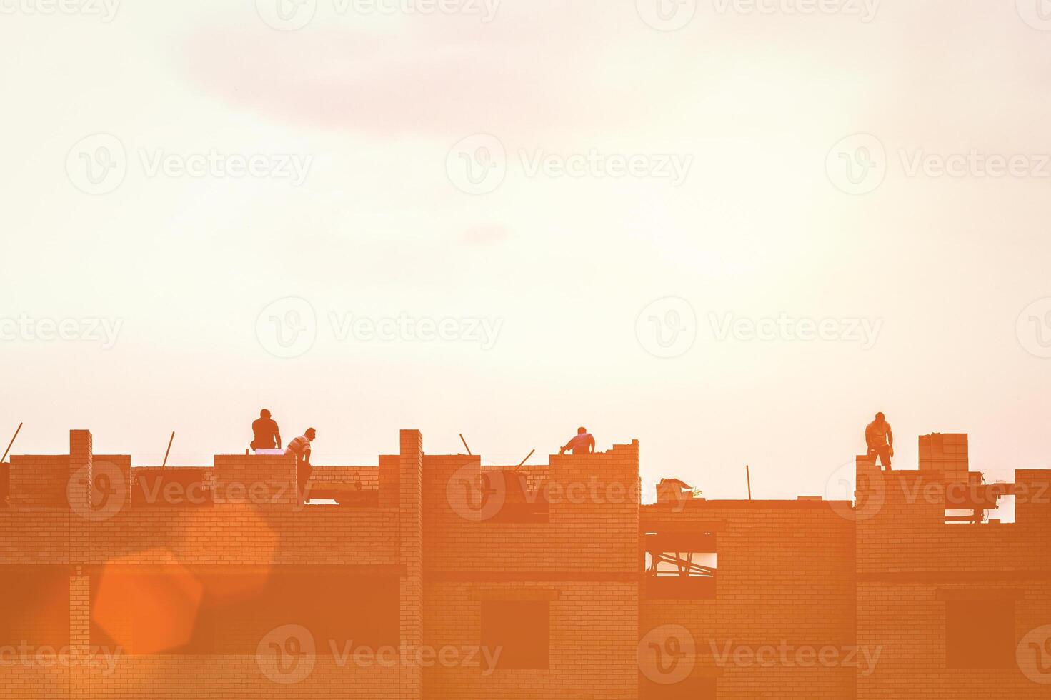 Silhouette of a team of construction workers constructing a building against the background of a sunset sky. photo